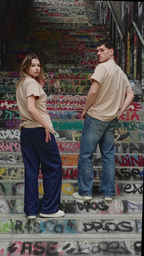 Mannequins homme et femme de dos, portant le t-shirt beige Indieviduals, avec comme décor un escalier rempli de tags. 